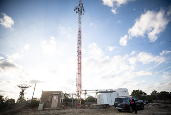 A photo of a red and white radio tower sticking up into a blue clouded sky.