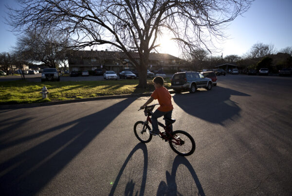 A young boy wearing an orange shirt and jeans rides his bike in the street