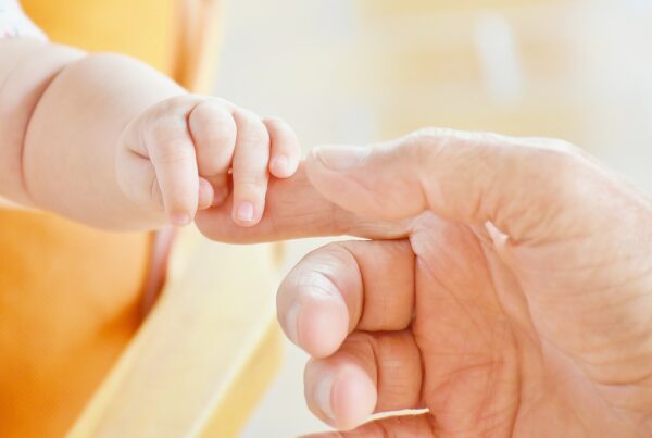A yellow and orange-tinged photo of a baby holding the finger of an adult.